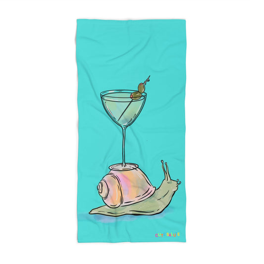 A turquoise rectangular towel or blanket featuring a whimsical illustration of a martini glass with olives and a snail on a pink shell, shown on a plain white background.