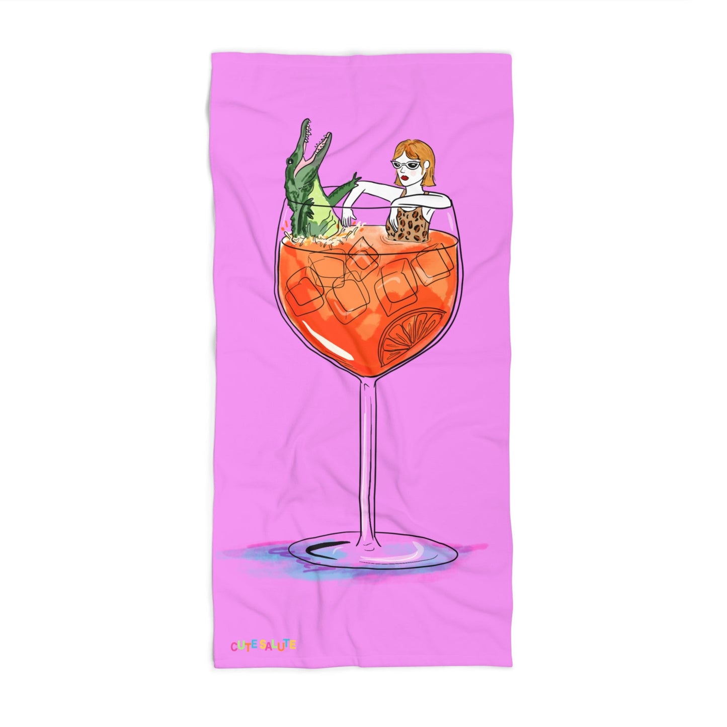 A pink rectangular towel featuring a whimsical illustration of a woman with orange hair sitting inside a large orange cocktail glass with an alligator, shown on a white background.