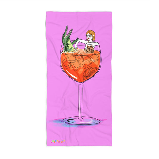 A rectangular pink towel featuring a whimsical illustration of a woman sitting inside a large orange cocktail glass with ice, on a white background.
