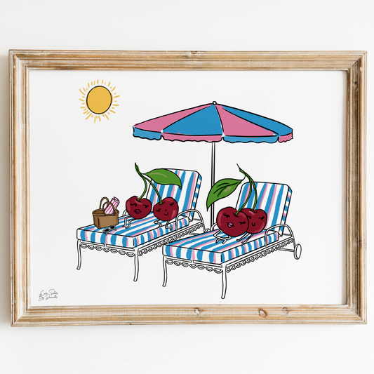 A framed art print featuring a whimsical illustration of two lounge chairs under a pink and blue striped umbrella, decorated with red cherries, on a white background with a light wood frame.