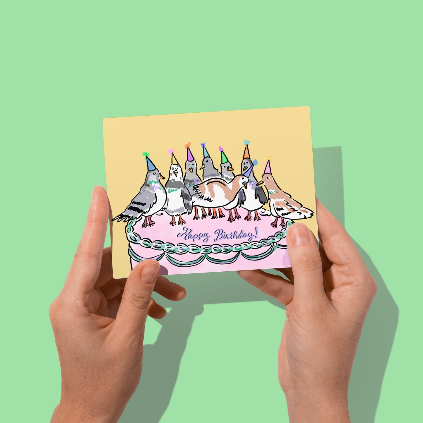 Hands holding a birthday card with cake illustration on a green background
