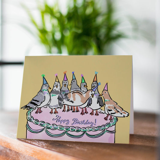 Greeting card with birthday cake and birds design on a wooden surface.