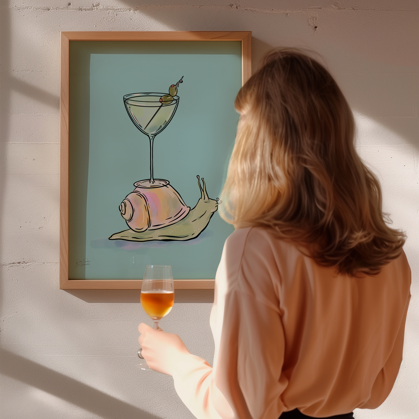 A woman stands with her back to the camera, holding a glass of amber liquid and looking at a framed art print on a white wall. The print shows a stylized illustration of a snail carrying a martini glass with an olive on a light blue background.