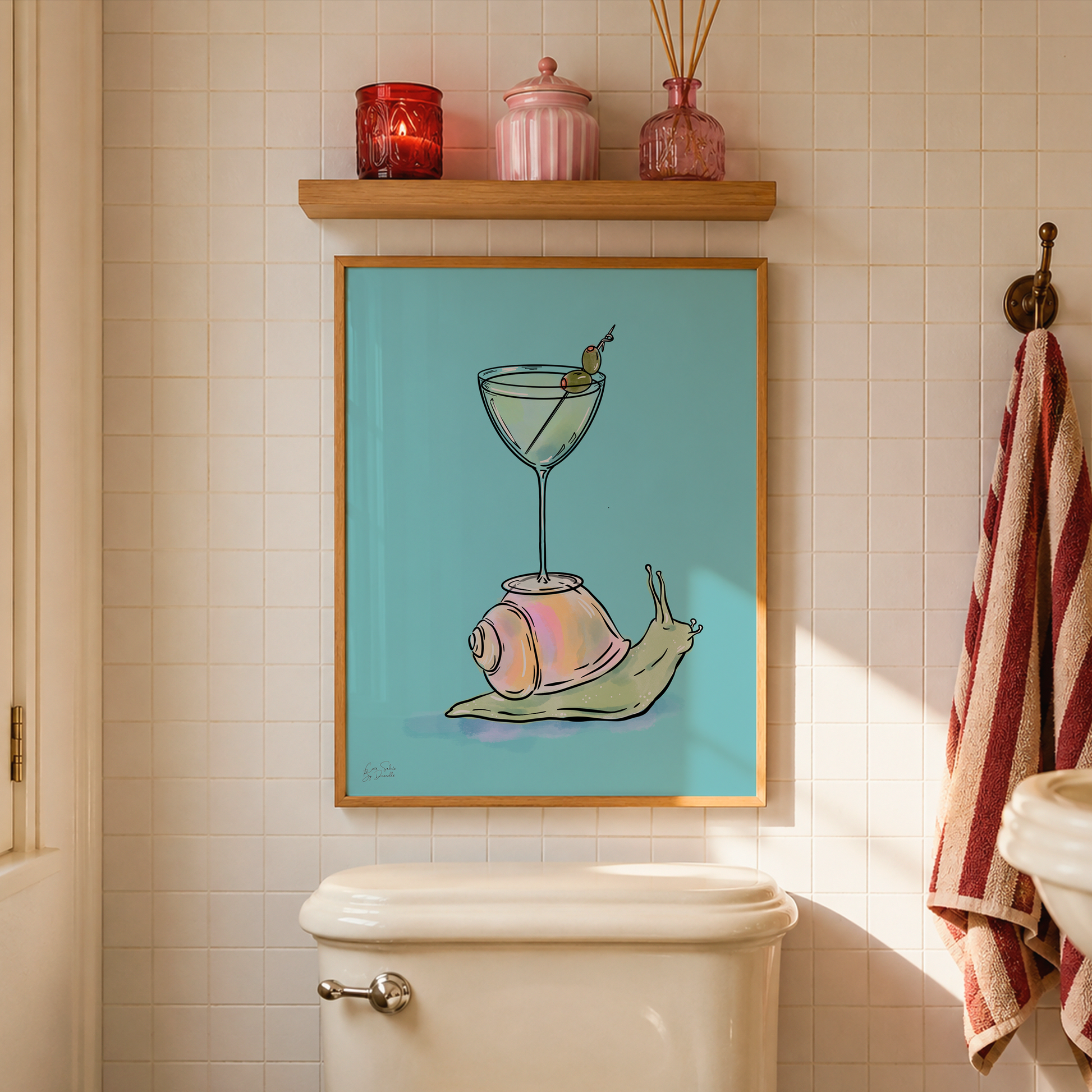 A framed art print featuring a whimsical illustration of a snail carrying a martini glass on its shell, displayed on a bathroom wall above a toilet with a wooden shelf and decorative items in the background.