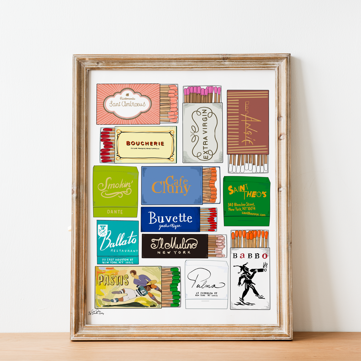 A framed art print featuring a collage of vintage NYC matchbook designs and logos, displayed on a light wood surface against a white wall.
