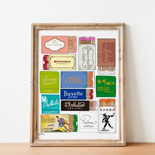 A framed art print featuring a collage of vintage NYC matchbook designs and logos, displayed on a light wood surface against a white wall.