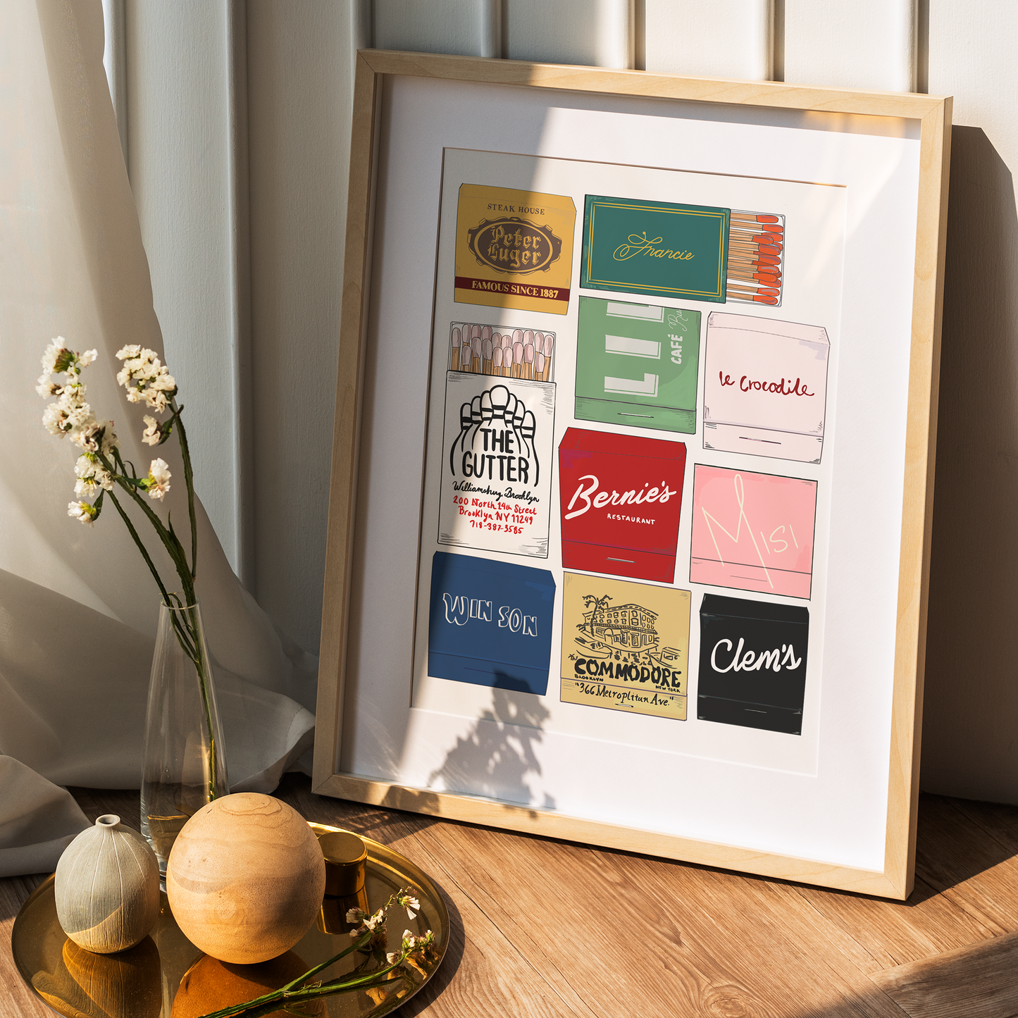 Framed print of vintage product labels on a wooden surface with decorative items.