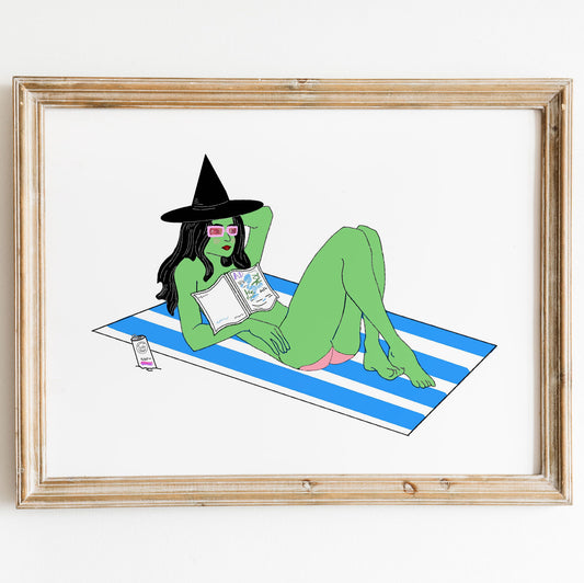 framed illustration of a witch with green skin, sitting on a beach towel